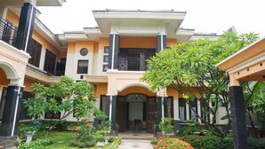 A two-story building with a central entrance, surrounded by a garden with various plants and flowers. - Green Surabaya Homey (Surabaya)