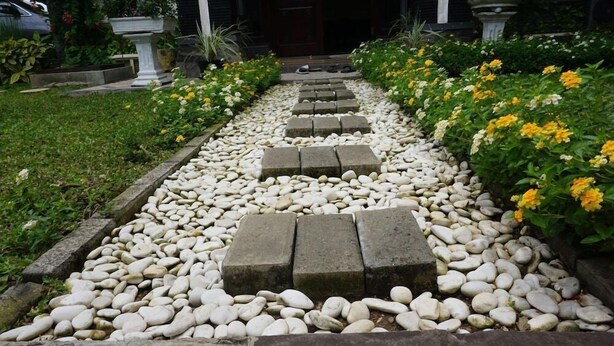 A garden pathway with white pebbles and stepping stones leading to a door. - Green Surabaya Homey (Surabaya)