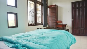 A bedroom with a bed, a wardrobe, a window with decorative bars, and a door. - Green Surabaya Homey (Surabaya)