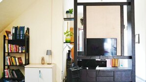 A living room with a bookshelf, a small cabinet, a TV, and a coffee machine. - Green Surabaya Homey (Surabaya)