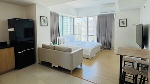 Una habitación de hotel moderna con cama, sof á, mesa de comedor con sillas, televisión y un minibar.