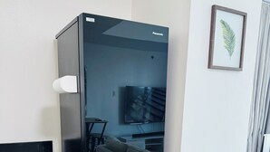 Una cocina compacta con un refrigerador negro, un armario de madera, un sofá color beige y una planta enmarcada en la pared.
