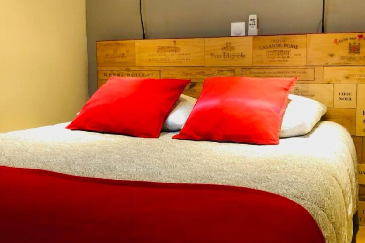 Un lit avec une tête de lit blanche et des oreillers rouges, placé devant un fond constitué de panneaux en bois ornés de texte.