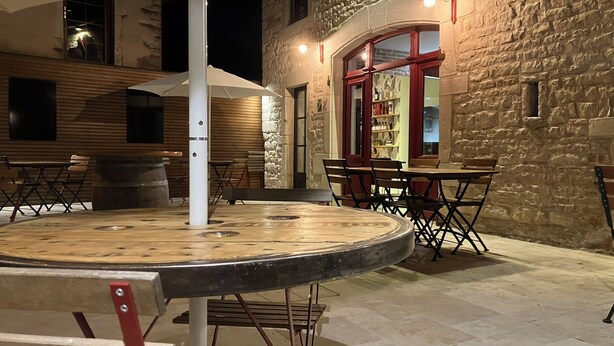 An outdoor dining area with a round wooden table, metal chairs, and a white umbrella. - L'aubergiste (Corcelles-les-Arts)