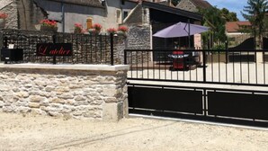 A stone building with a red-tiled roof, a sign reading "Latcherie," and a fenced outdoor area with a table and chairs. - L'aubergiste (Corcelles-les-Arts)