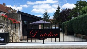 A stone wall with a sign reading "L'atelier" in front of a building with a black roof and a glass door. - L'aubergiste (Corcelles-les-Arts)