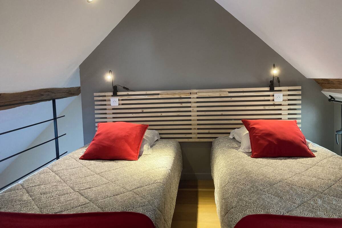 Une chambre avec deux lits, chacun doté d’un oreiller rouge, d’une tête de lit en bois à lattes et d’une petite table avec une lampe.