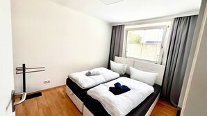 Une petite chambre à coucher, bien rangée, avec un lit simple, une fenêtre avec des rideaux et un radiateur.