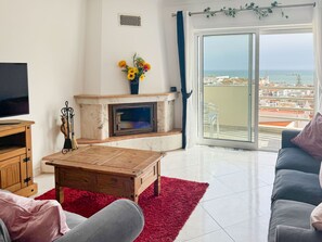 Una sala de estar con chimenea, televisión y vista al mar.