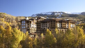Een hotel met meerdere verdiepingen met een centrale binnenplaats, omringd door herfstkleuren en met op de achtergrond besneeuwde bergtoppen.