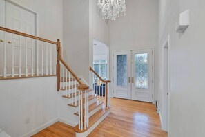 Un pasillo amplio con escaleras de madera, puertas blancas y un candelabro.