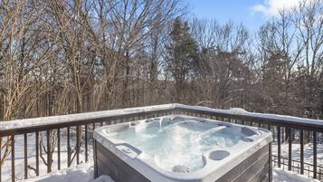 A hot tub surrounded by snow-covered trees and a wooden deck.