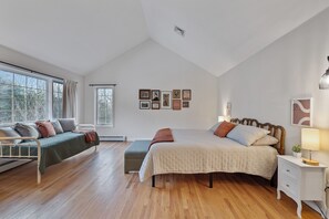 A bedroom with a large bed, a sofa, a bedside table, and a window.