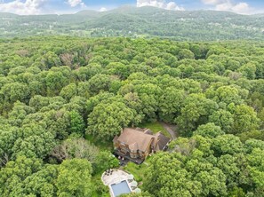 Una casa grande rodeada de un bosque frondoso, con piscina y zona de estar al aire libre.