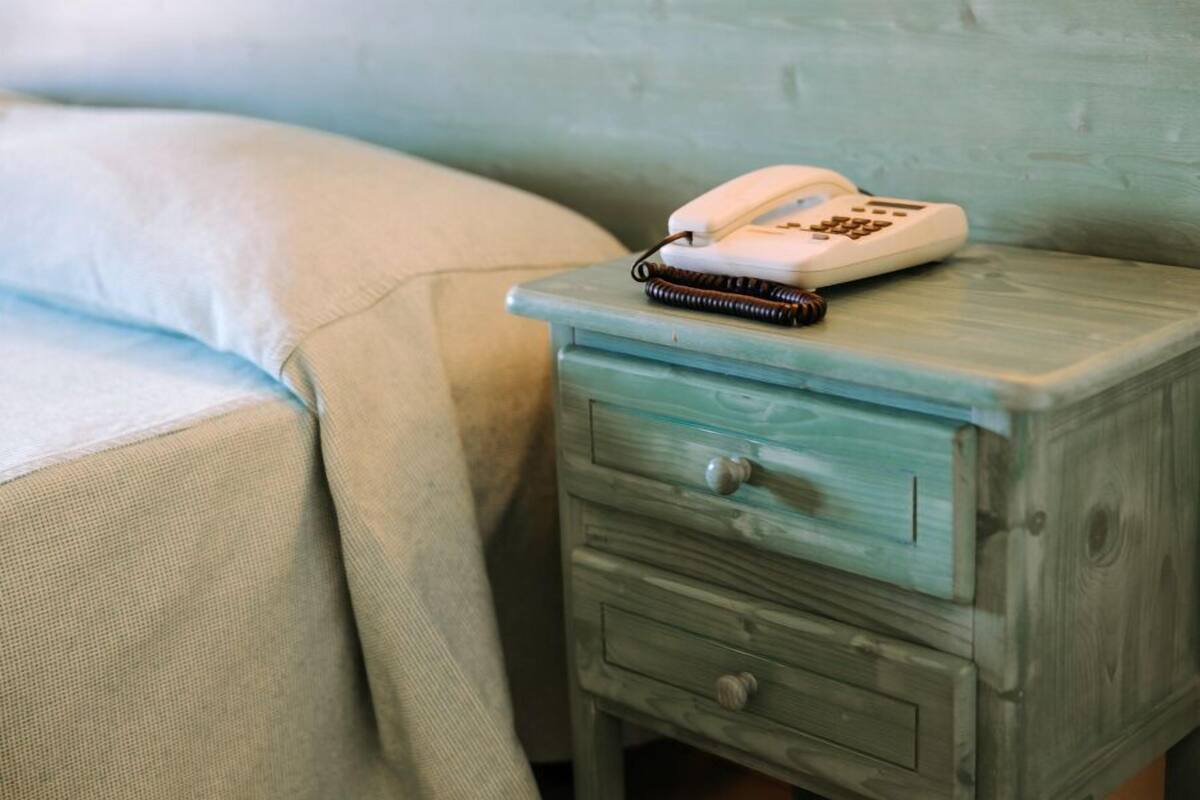 A small wooden nightstand with a drawer and a telephone.