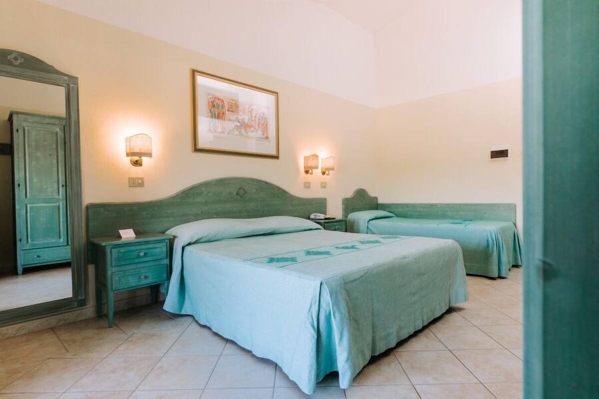 A room with two beds, a nightstand, a mirror, and wall-mounted lights.