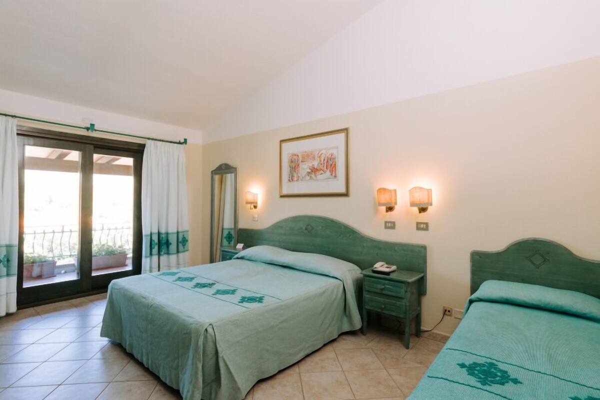 A hotel room with a bed, a nightstand, a mirror, and a window with curtains.