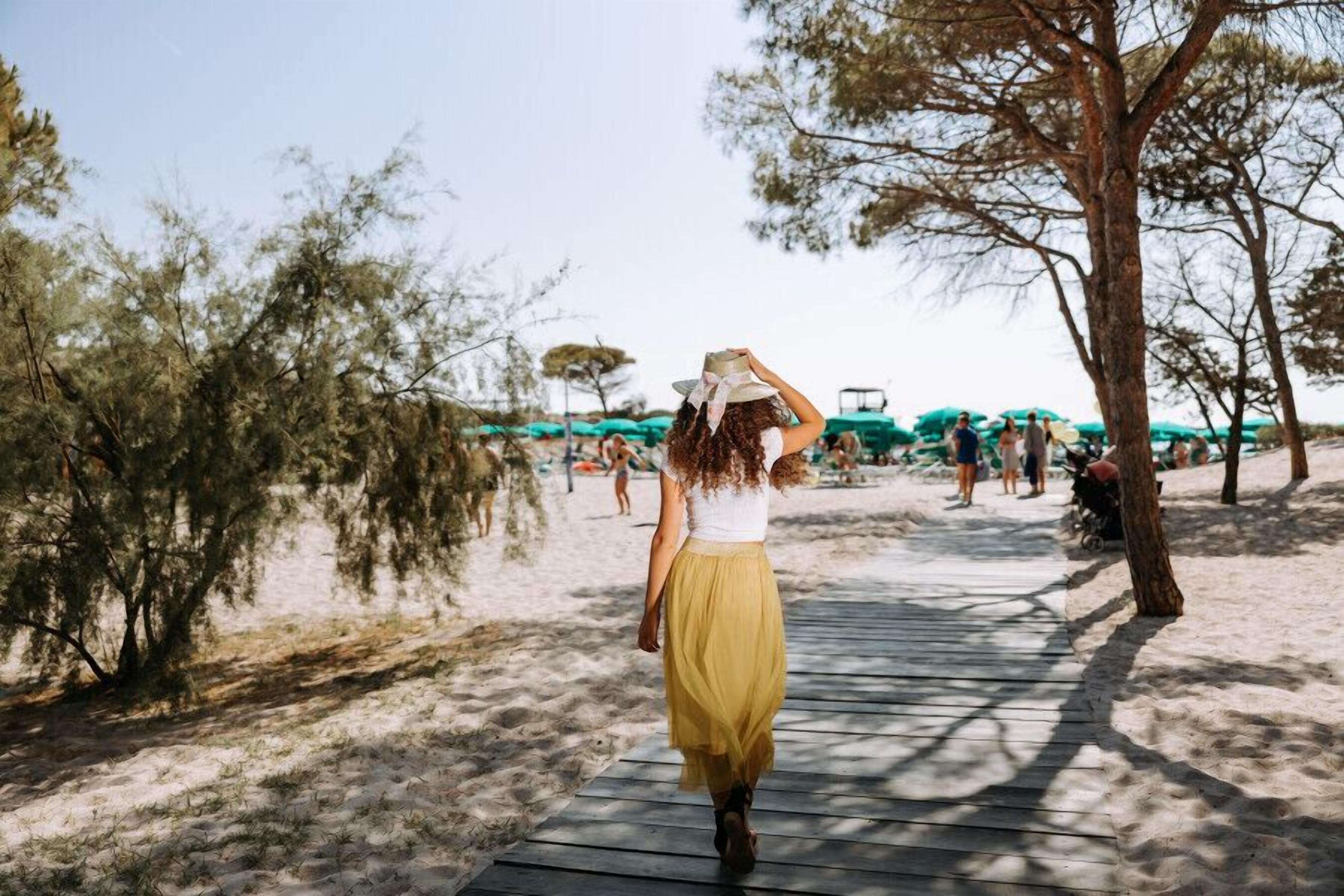 Un sentier menant à une plage bordée d’arbres et dotée de parasols.