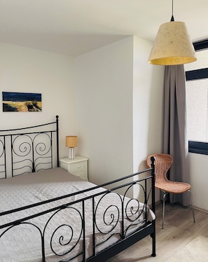 Un dormitorio con cama, mesita de noche, silla, lámpara colgante y un cuadro en la pared.