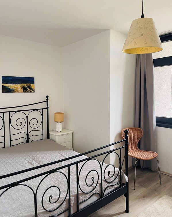Un dormitorio con cama, mesita de noche, silla, lámpara colgante y un cuadro en la pared.