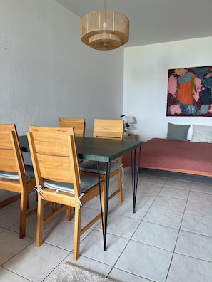 Un comedor con mesa y sillas, una lámpara colgante, un cuadro en la pared y un sofá con cojines.