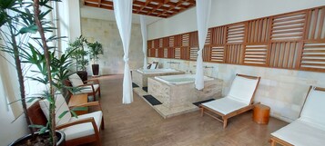 Uma área de spa com painéis de madeira, uma planta grande e um espaço de estar com cadeiras e um banco.