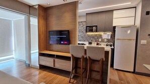A modern kitchen with a built-in TV, wooden panel wall, and bar stools.