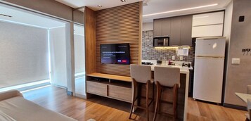 Cozinha moderna com televisão integrada, painel de parede de madeira e banquetas de bar.