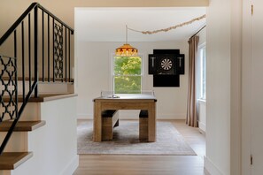 A room with a wooden table, a chandelier, a dartboard, and a window with curtains.