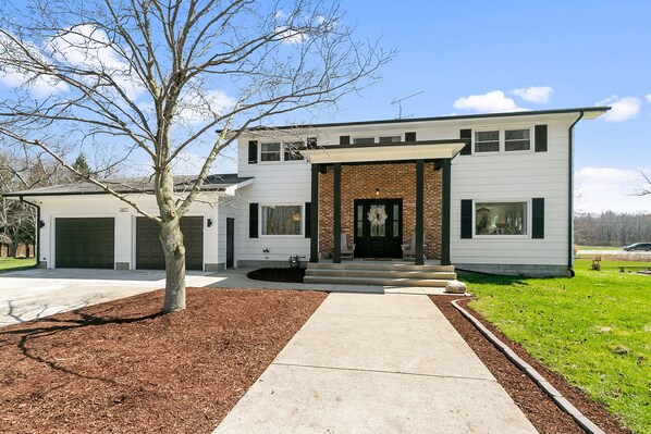 A modern two-story house with a brick facade, a front porch, and a driveway leading to a garage.