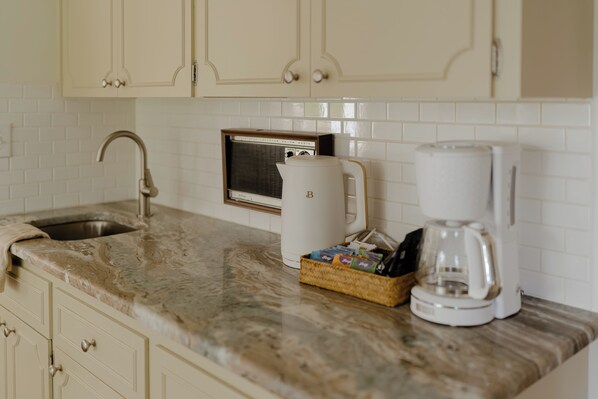 A kitchen with a marble countertop, a coffee maker, a kettle, and a basket of coffee pods.