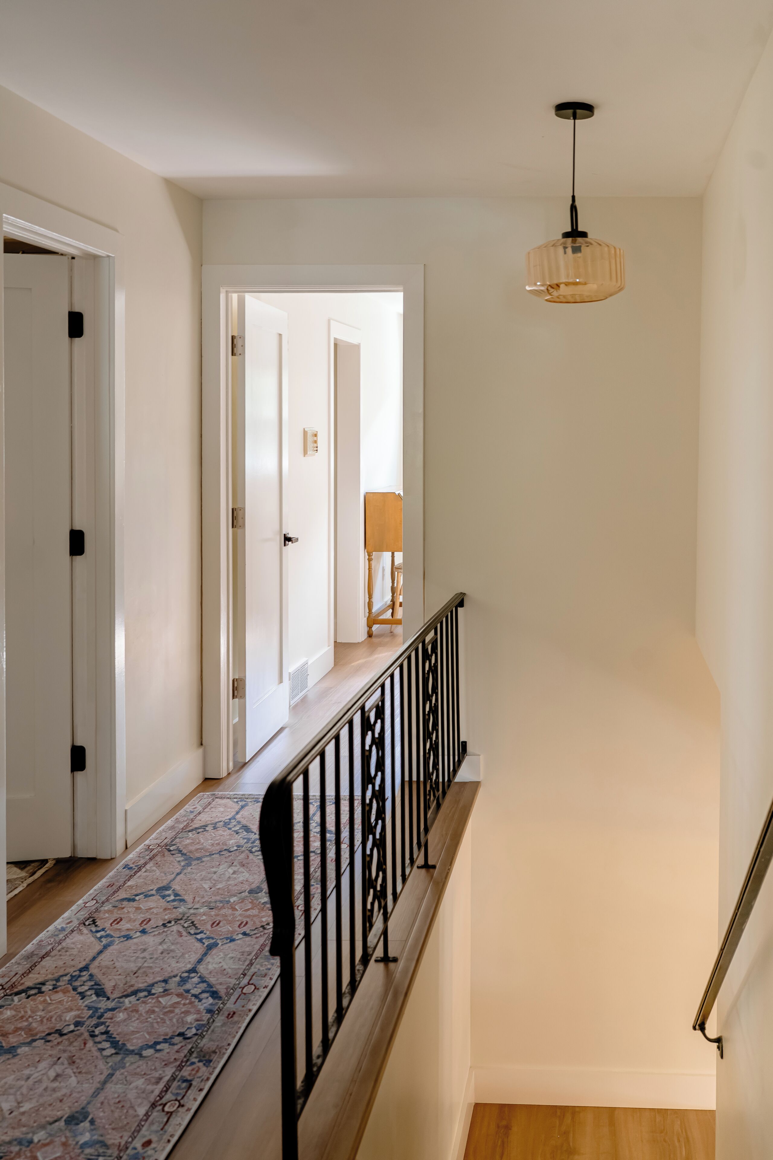 A staircase with a patterned carpet, a black railing, and a hanging light fixture.