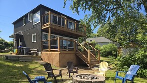 Ein zweistöckiges Haus mit einer Terrasse, Sitzgelegenheiten im Freien und einer Feuerstelle.