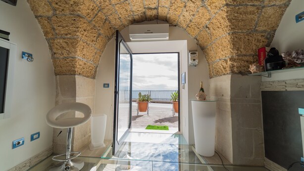 A modern interior with a stone archway leading to a balcony with potted plants. - SUITE ORTIGIA SEA VIEW (Siracusa)