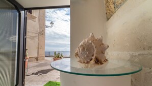 A glass table with a seashell centerpiece, a view of the sea through a window, and a potted plant on a balcony. - SUITE ORTIGIA SEA VIEW (Siracusa)
