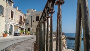 A coastal street with buildings, a paved sidewalk, and a railing overlooking the sea. - SUITE ORTIGIA SEA VIEW (Siracusa)
