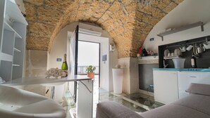 A modern kitchen with stone arch ceilings, a glass dining table, and a built-in oven. - SUITE ORTIGIA SEA VIEW (Siracusa)