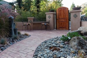 Eine Terrasse mit gefliestem Boden, zwei Stühlen, einer Holztür und einer Wand mit geometrischem Muster.