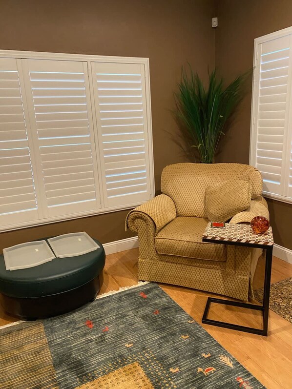 A living room with a beige sofa, a small side table, a green ottoman, and a patterned rug.