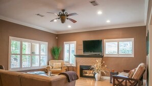 Un salon doté d’une cheminée, d’un ventilateur de plafond et d’un téléviseur fixé au-dessus de la cheminée.