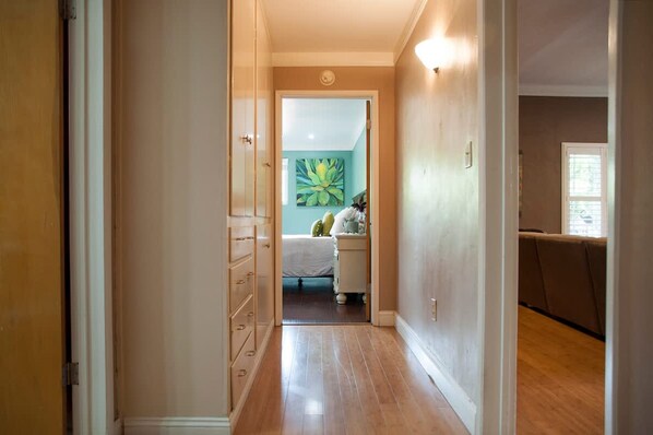 A hallway leading to a bedroom with a bed, a nightstand, and a painting on the wall.