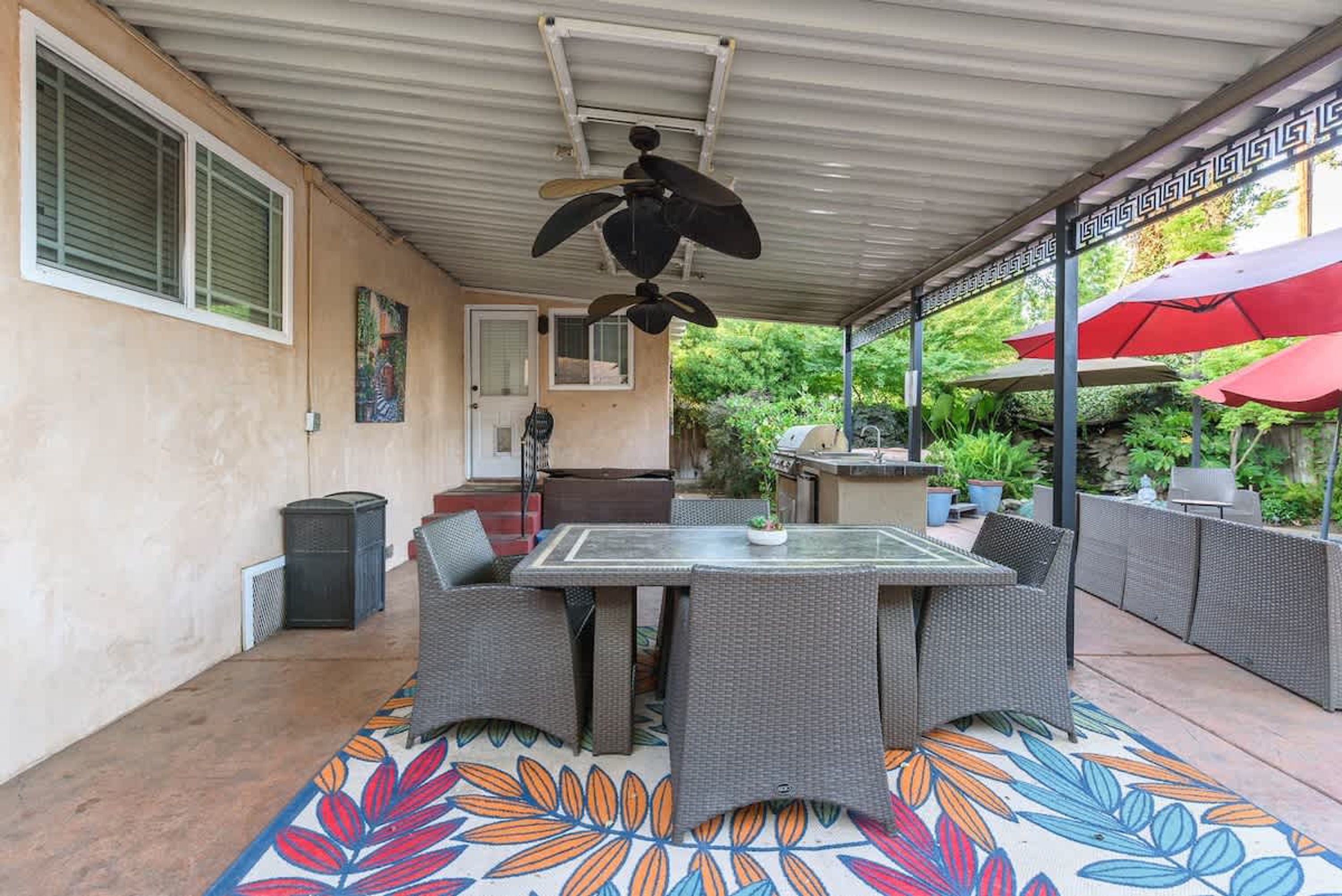 Un patio al aire libre con mesa y sillas, un ventilador de techo y una zona de barbacoa.