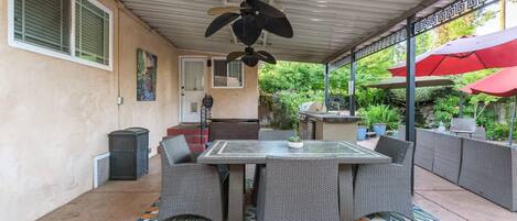 Un patio al aire libre con mesa y sillas, un ventilador de techo y una zona de barbacoa.