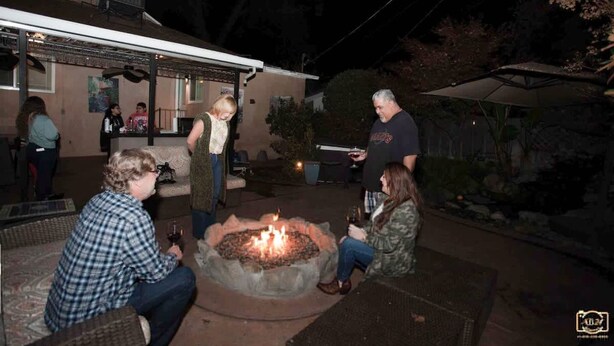 Un área de estar al aire libre con una chimenea, rodeada de mobiliario de patio y un porche cubierto.