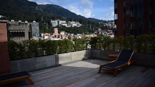 Une terrasse sur le toit, dotée de chaises longues et d’une petite table, offrant une vue sur le paysage urbain, avec des montagnes en arrière-plan.