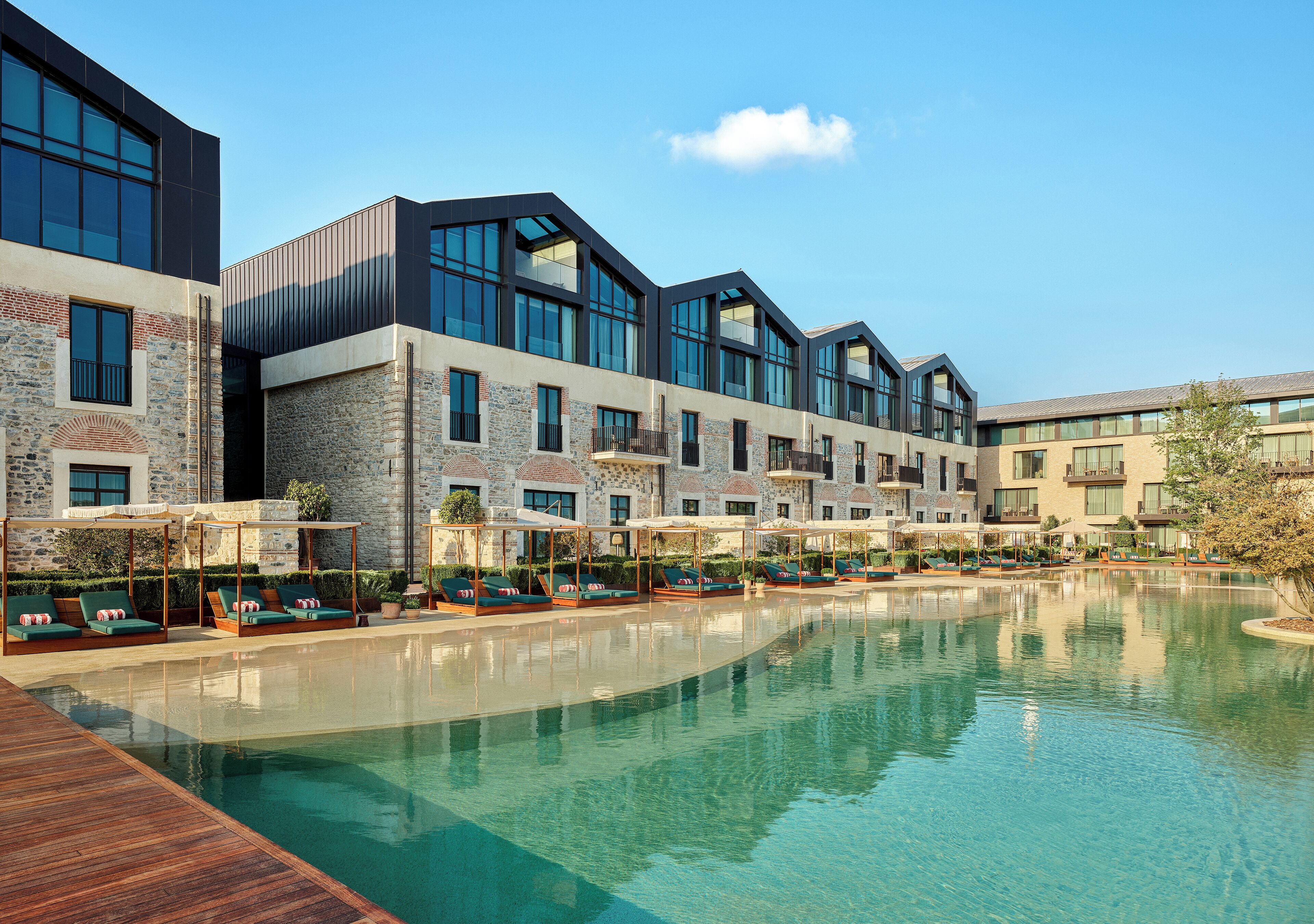 A modern hotel with a pool, outdoor seating, and a stone facade.