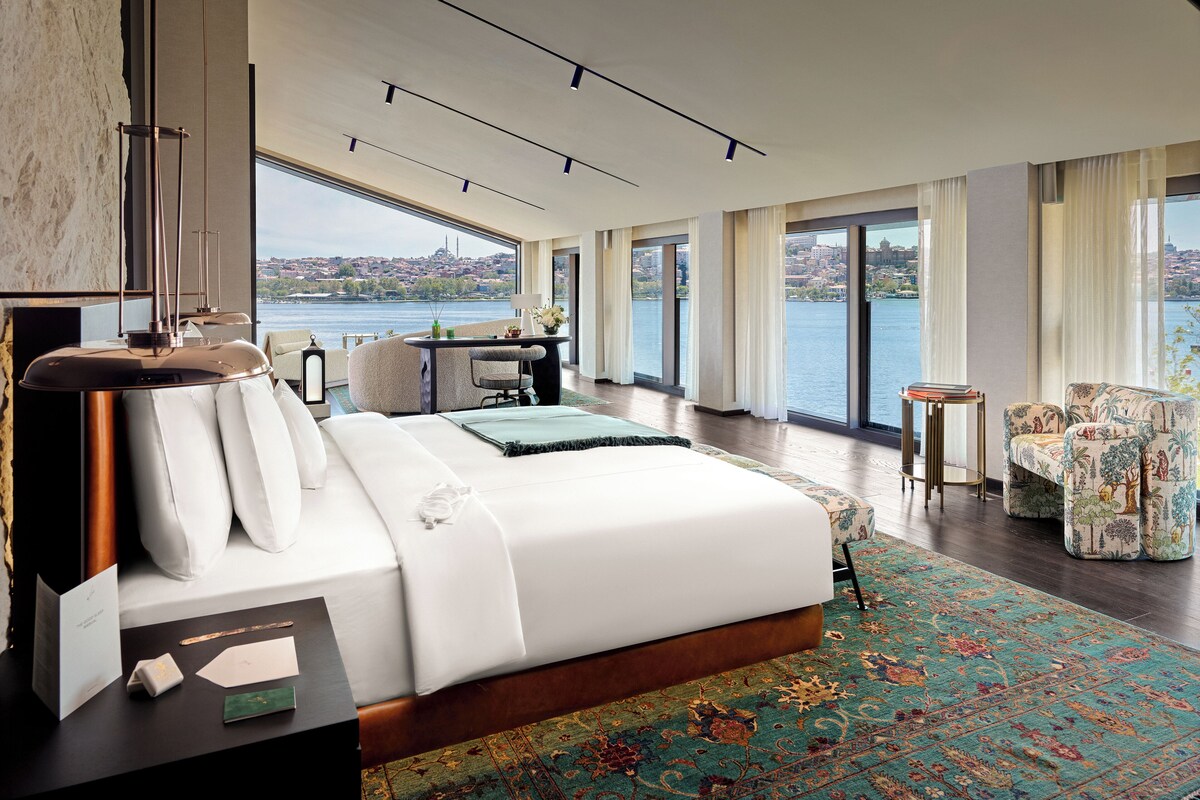 Une chambre d’hôtel moderne dotée d’un grand lit, d’un bureau et offrant une vue sur le paysage urbain et l’eau.