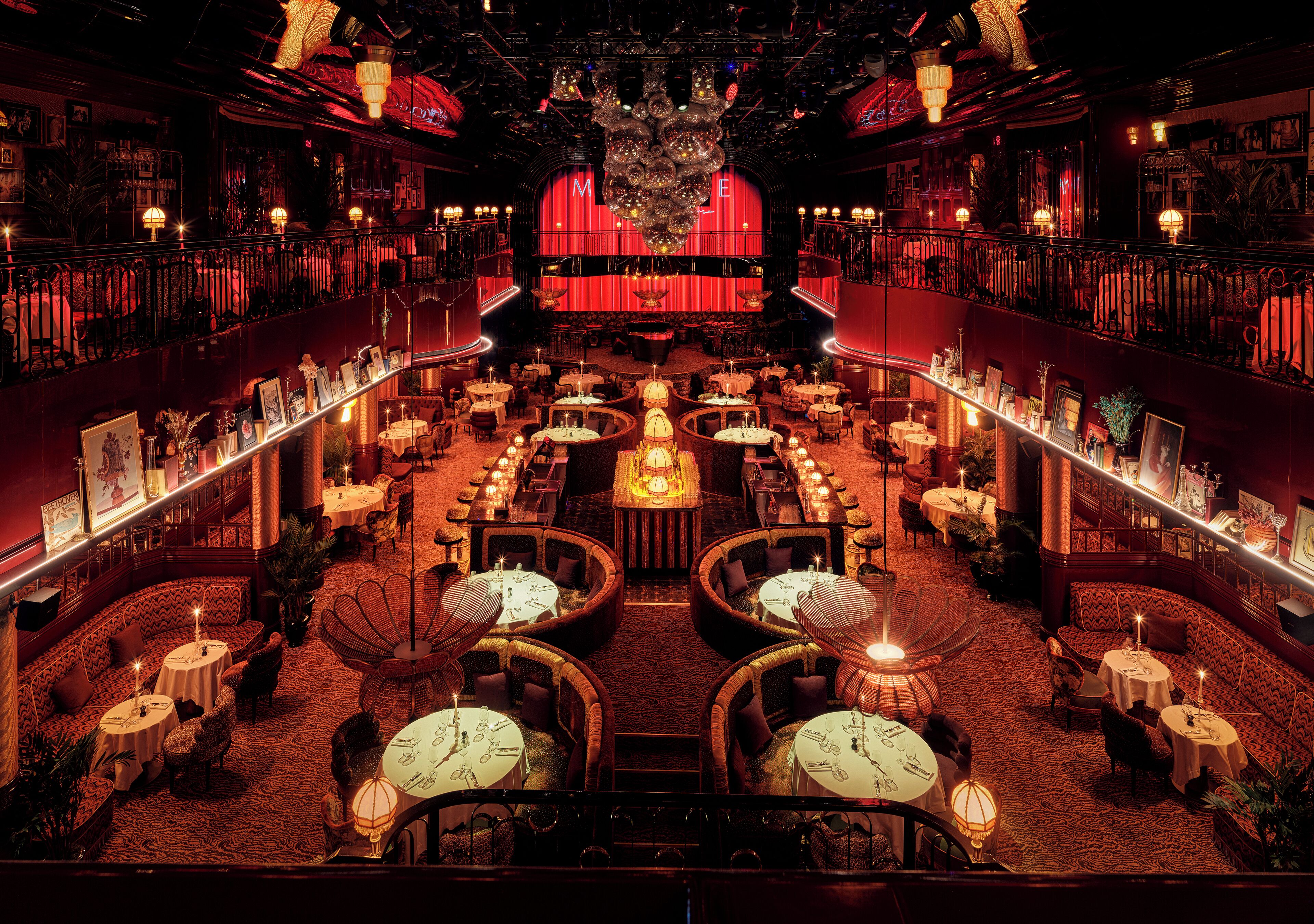 Un hall d’hôtel luxueux, doté d’une scène centrale, de plusieurs espaces aménagés pour s’asseoir et d’un décor de fond rouge.
