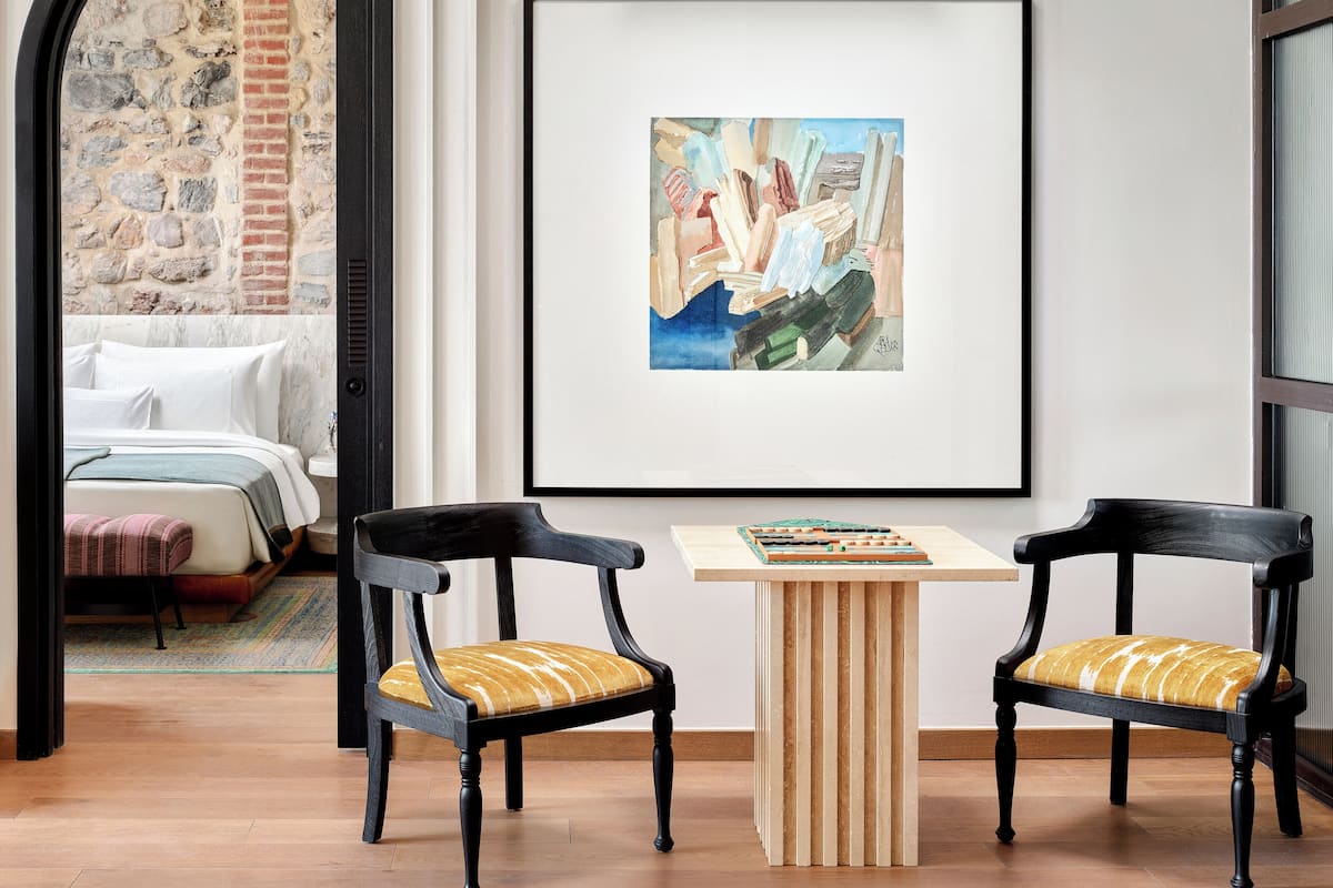 Ein modernes Zimmer mit einem Bett, zwei Stühlen, einem kleinen Tisch und einem gerahmten Kunstwerk an der Wand.