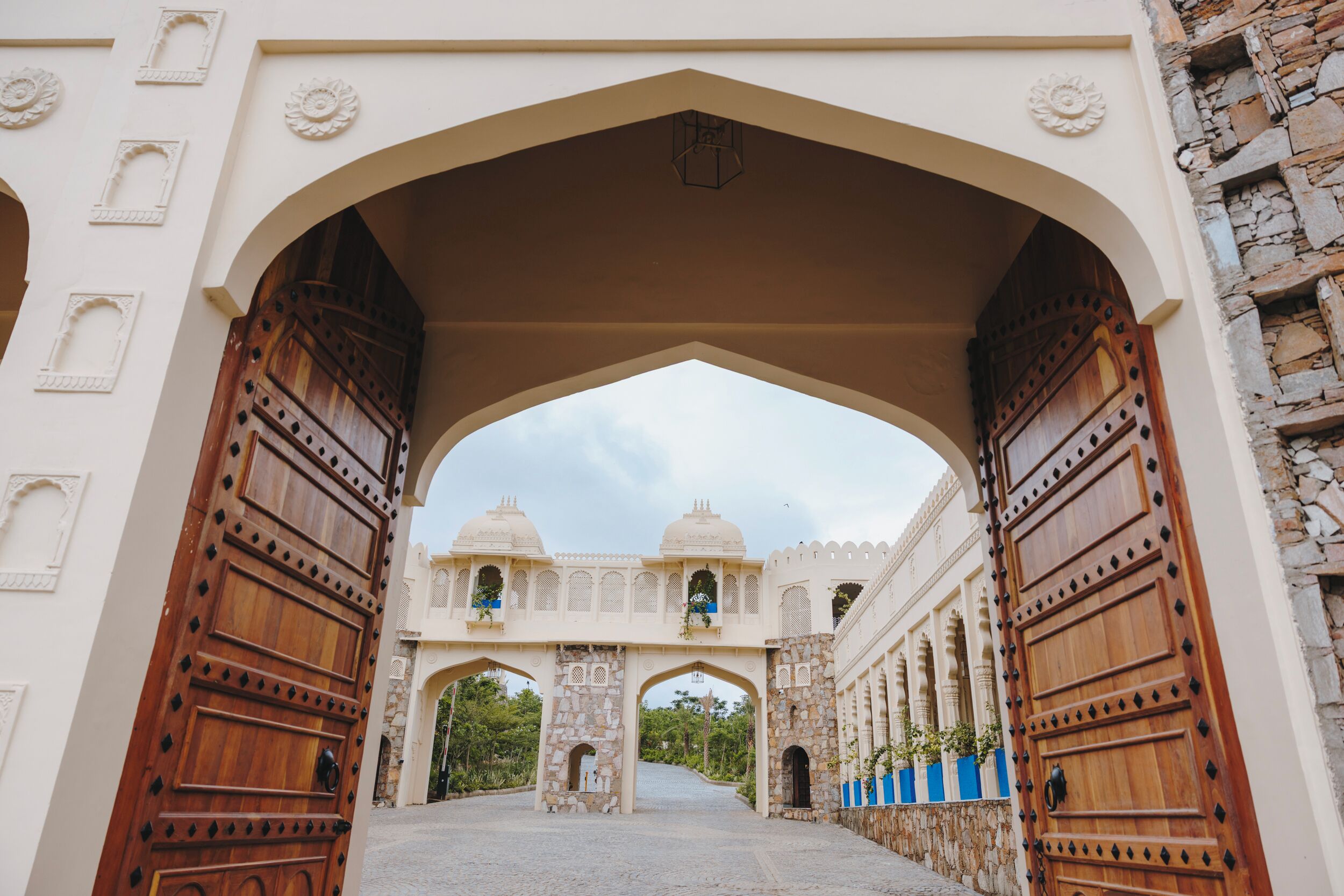 An arched entrance with large wooden doors and a view of a building with domes and arches.